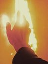 Crop anonymous person reaching out hand to flame during fire in orange light