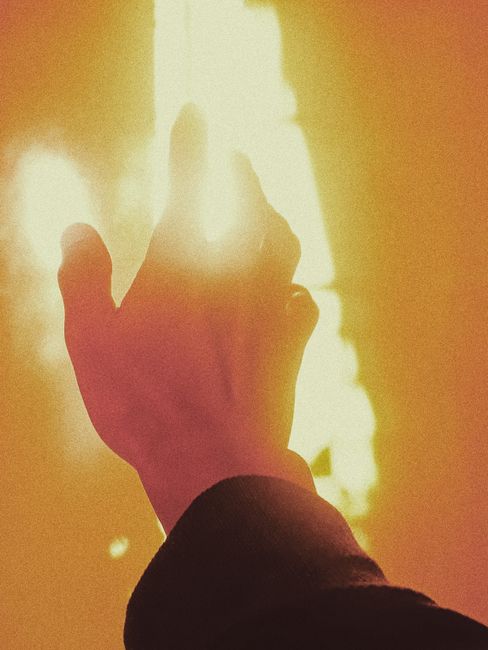 Crop anonymous person reaching out hand to flame during fire in orange light