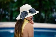 热带泳池边，一位戴时尚遮阳帽的女士侧面图