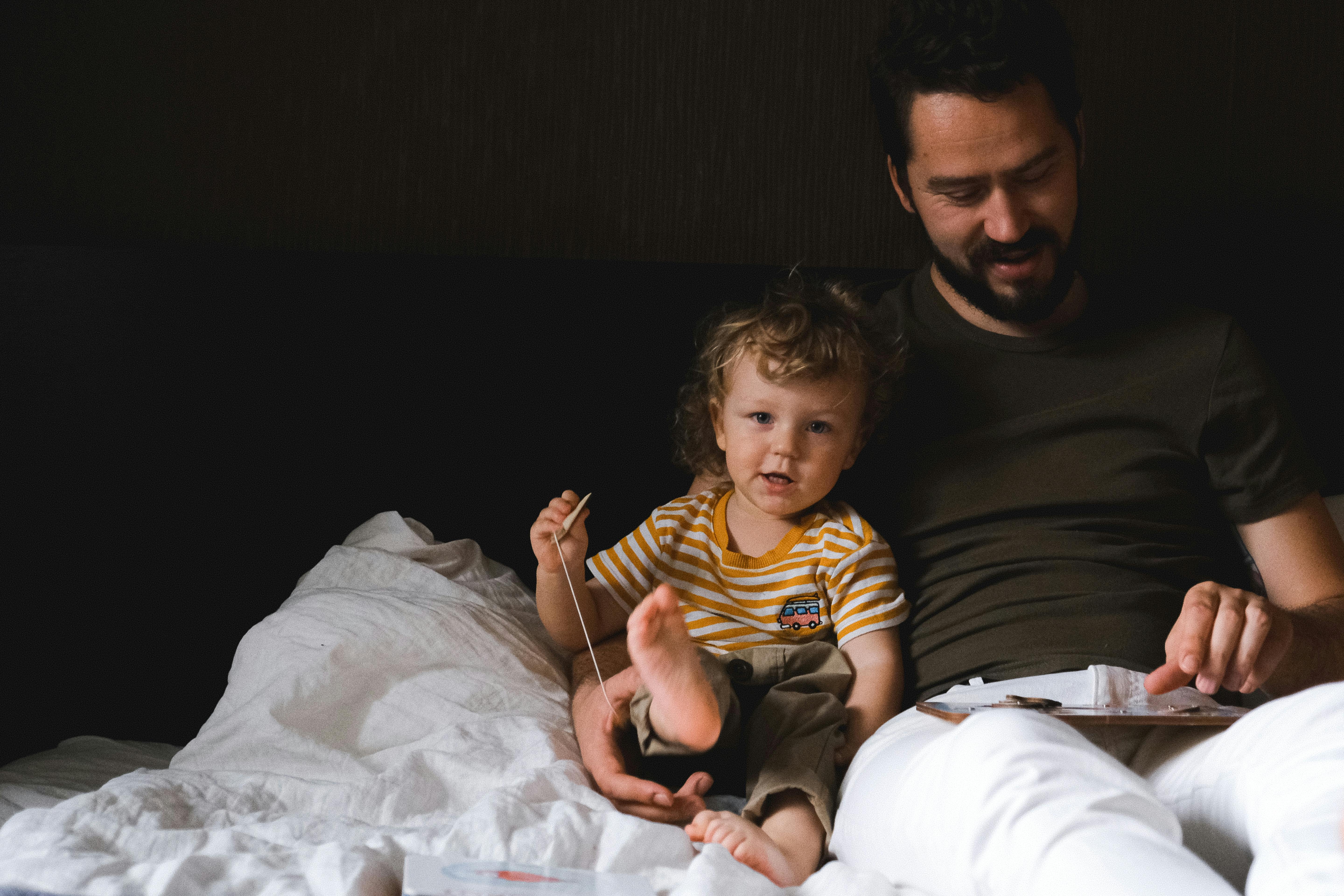 Father and child relaxing on a bed, enjoying a tender moment indoors with soft lighting.