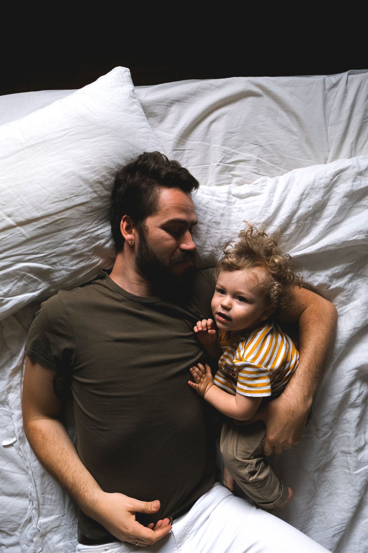 Father and young child asleep together in bed, showing why toddlers want to sleep next to their parents