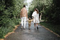 一对夫妇带着幼儿，在公园绿树成荫的小路上平静地散步