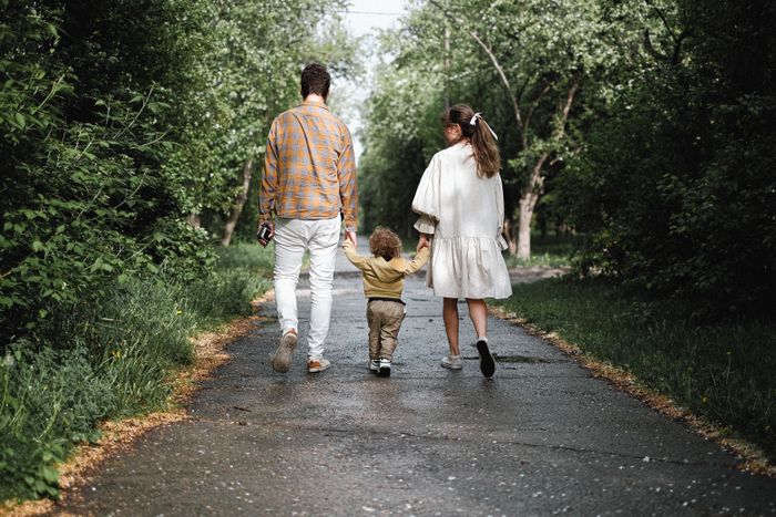 An adult and a child walking along a tree-lined path in a park