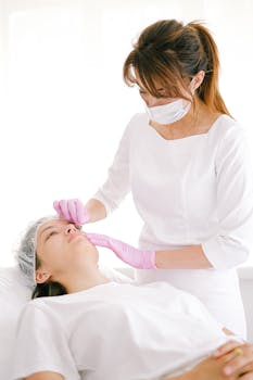 A beautician performs a cosmetic treatment on a woman in a clinical setting.