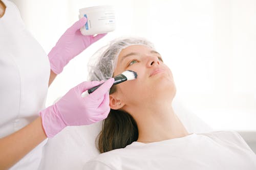 Woman Applying Ointment on Female Patient Face 