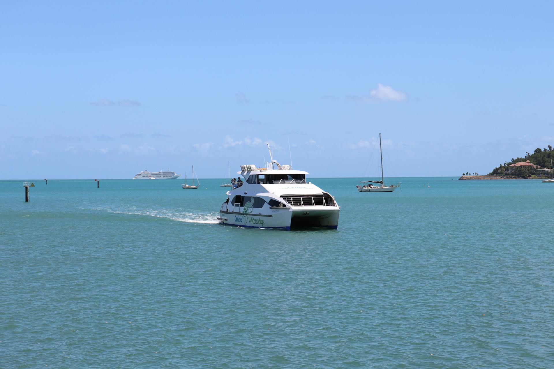 A white catamaran navigates turquoise waters under clear skies, with scenic Australian coastline in view.