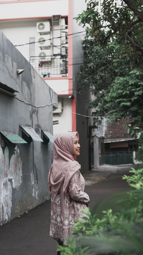 Free Young woman in patterned hijab smiling and standing outdoors with trees and buildings in the background. Stock Photo