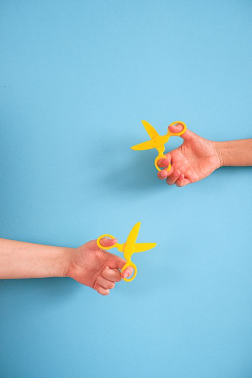 Free Two hands holding yellow scissors against a blue backdrop, featuring ample copy space. Stock Photo