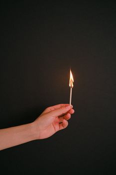 在黑暗的背景下，一只手持着燃烧的火柴，象征着点火与潜在的光芒