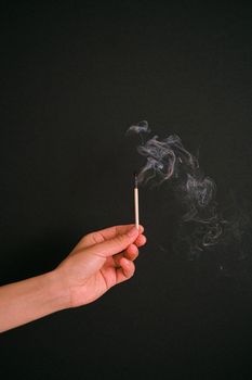 黑色背景下，一只手握着烧焦的火柴棍，烟雾缭绕