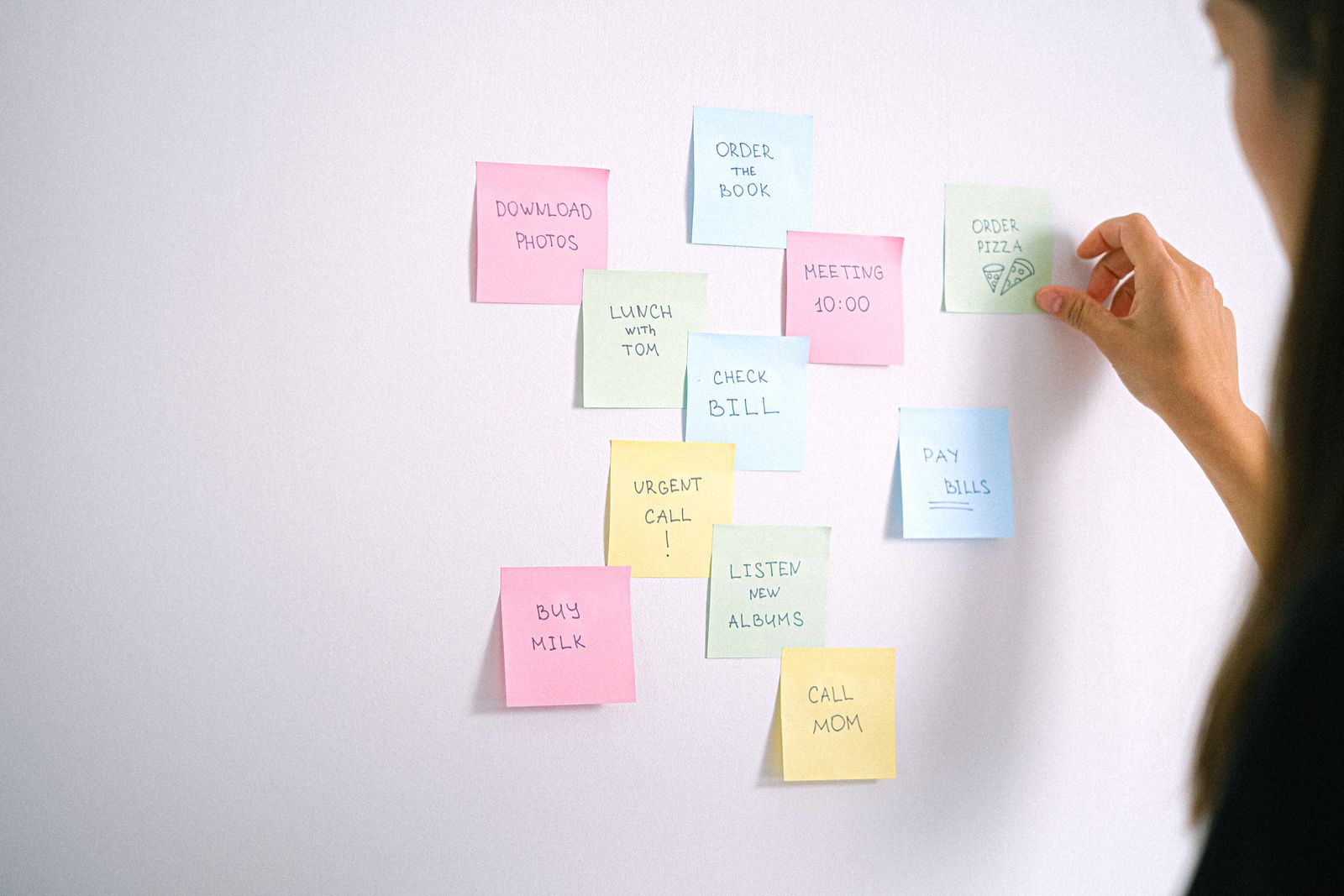 A hand places colored sticky notes with handwritten reminders on a white wall