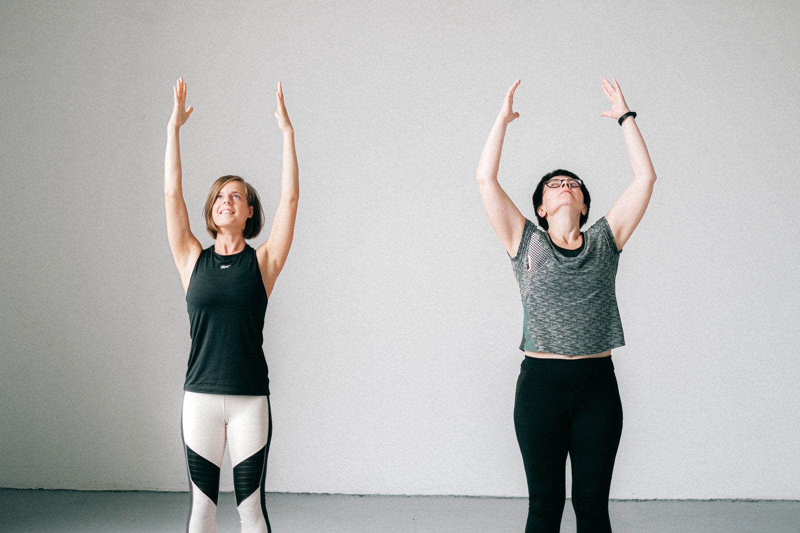 Two women standing with arms raised overhead during an indoor yoga session