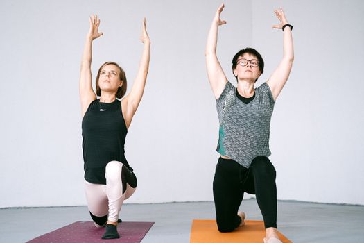 Two women engaging in yoga exercises indoors, focused on balance and mindfulness.