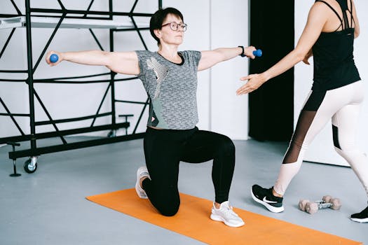 Two women working out with dumbbells on yoga mats in a modern gym setting, focusing on strength training.