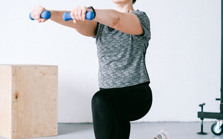 Adult woman exercising indoors with dumbbells on an orange mat for a healthy lifestyle.