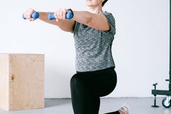 Adult woman exercising indoors with dumbbells on an orange mat for a healthy lifestyle.