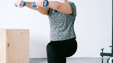Adult woman exercising indoors with dumbbells on an orange mat for a healthy lifestyle.