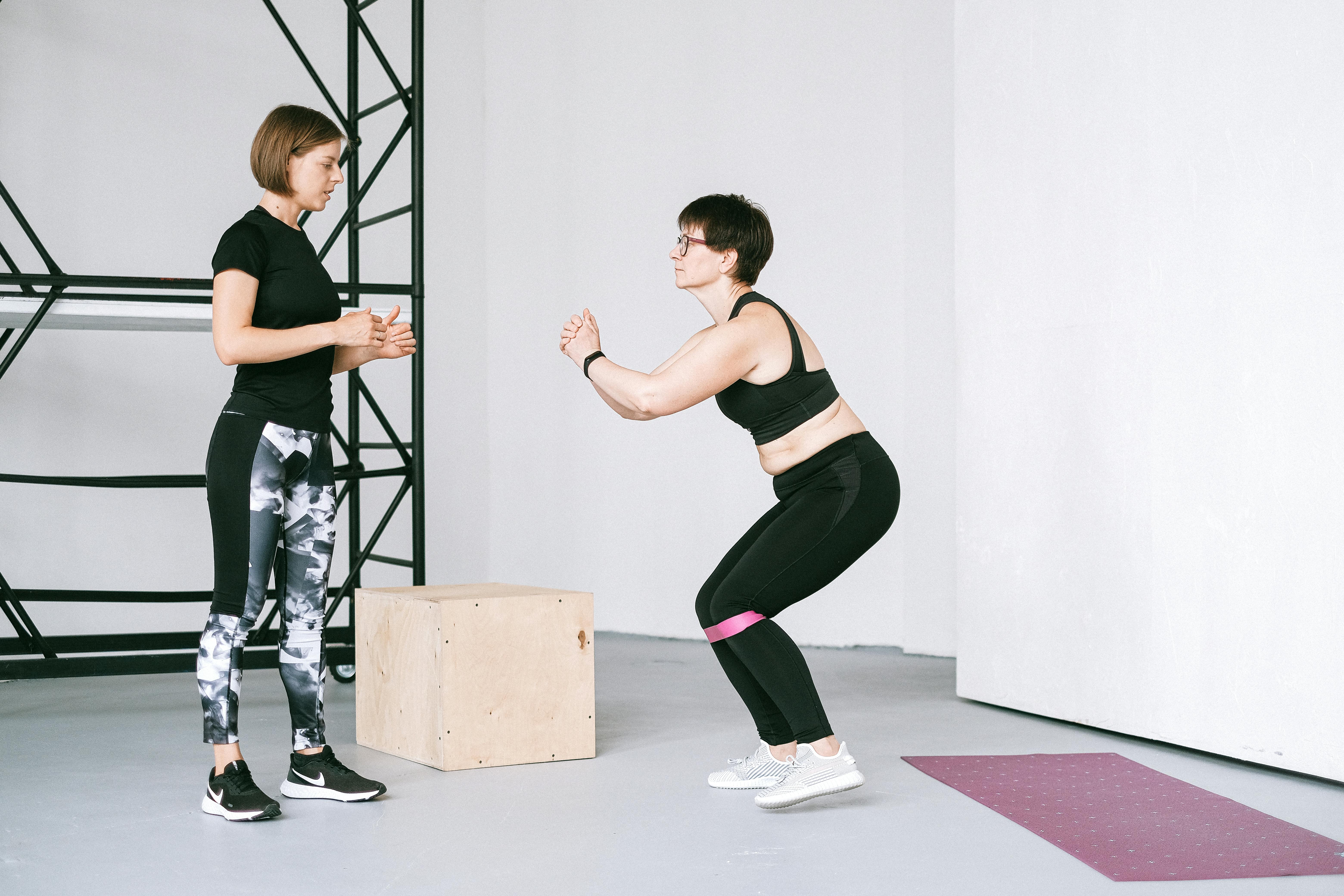 Two women engaging in a fitness workout with resistance bands at an indoor gym.