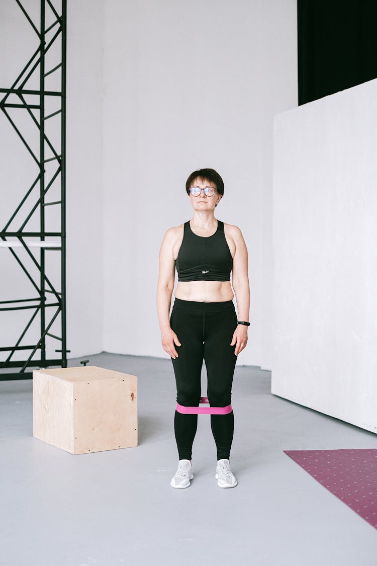 Woman Standing In Black Sports Bra And Leggings With Stretched Rubber Band On Her Legs