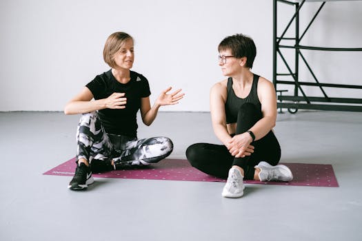Two women talking while sitting on yoga mats, focusing on fitness and health.