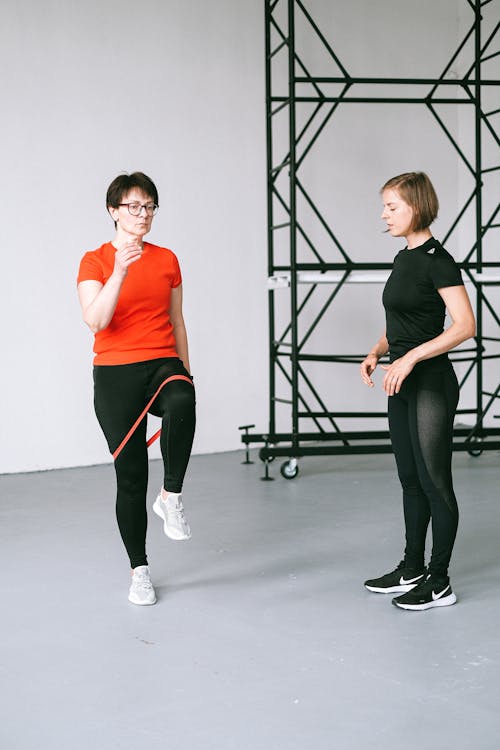 Woman in Orange Shirt and Black Leggings Sitting Beside Woman in Black Leggings