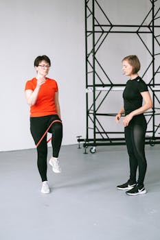 Two women exercising indoors with a resistance band, promoting a healthy and active lifestyle.