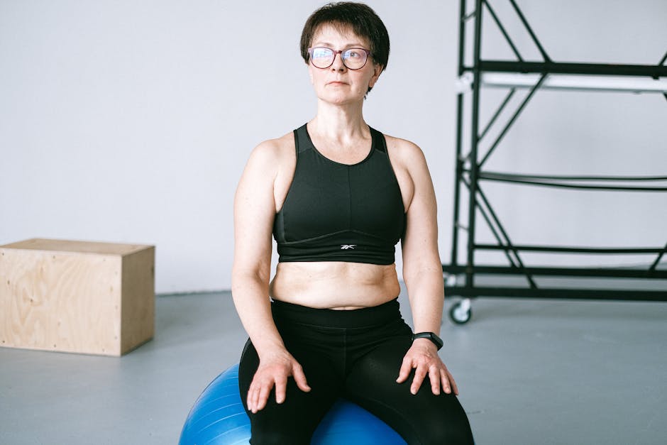 Middle-aged woman with eyeglasses exercising on a blue stability ball indoors.