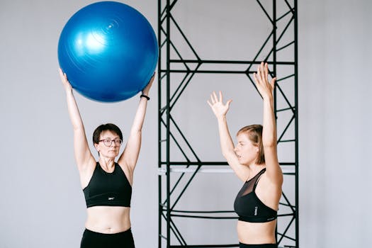 Two women exercising in a gym with a blue balance ball, promoting fitness and health.