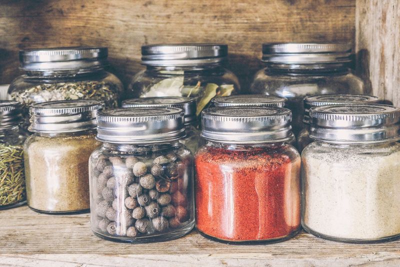 A collection of assorted spices in glass jars on a rustic wooden shelf for culinary use.