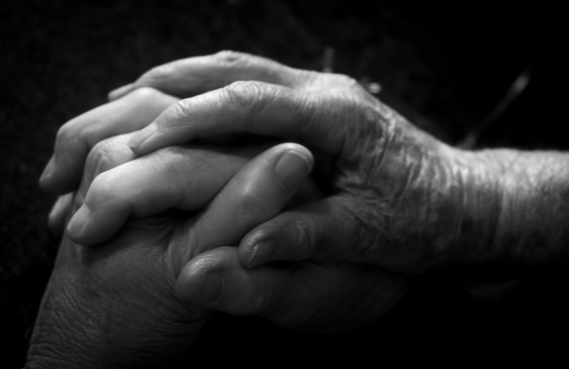 Close-up of two hands clasped together in a grayscale setting, evoking connection and care.