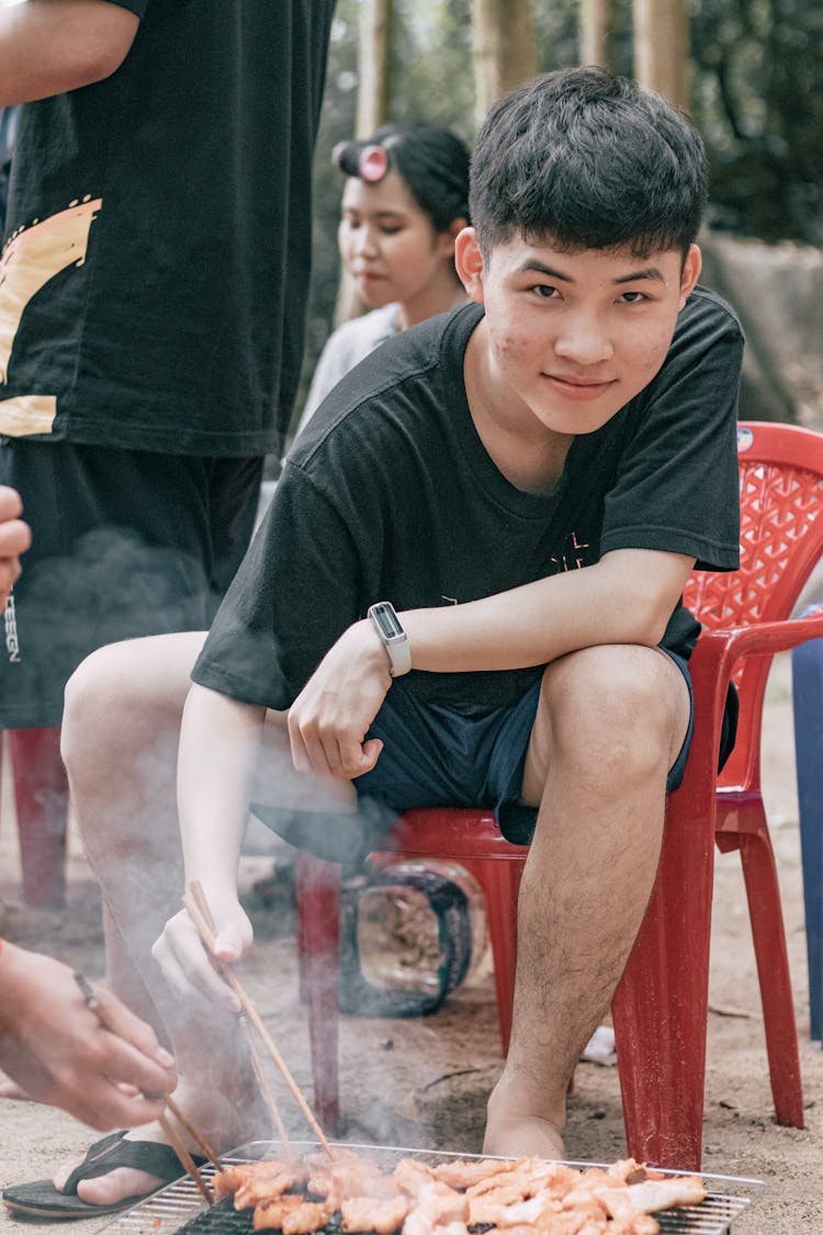 Smiling Asian Teenager Eating Meat In Campground