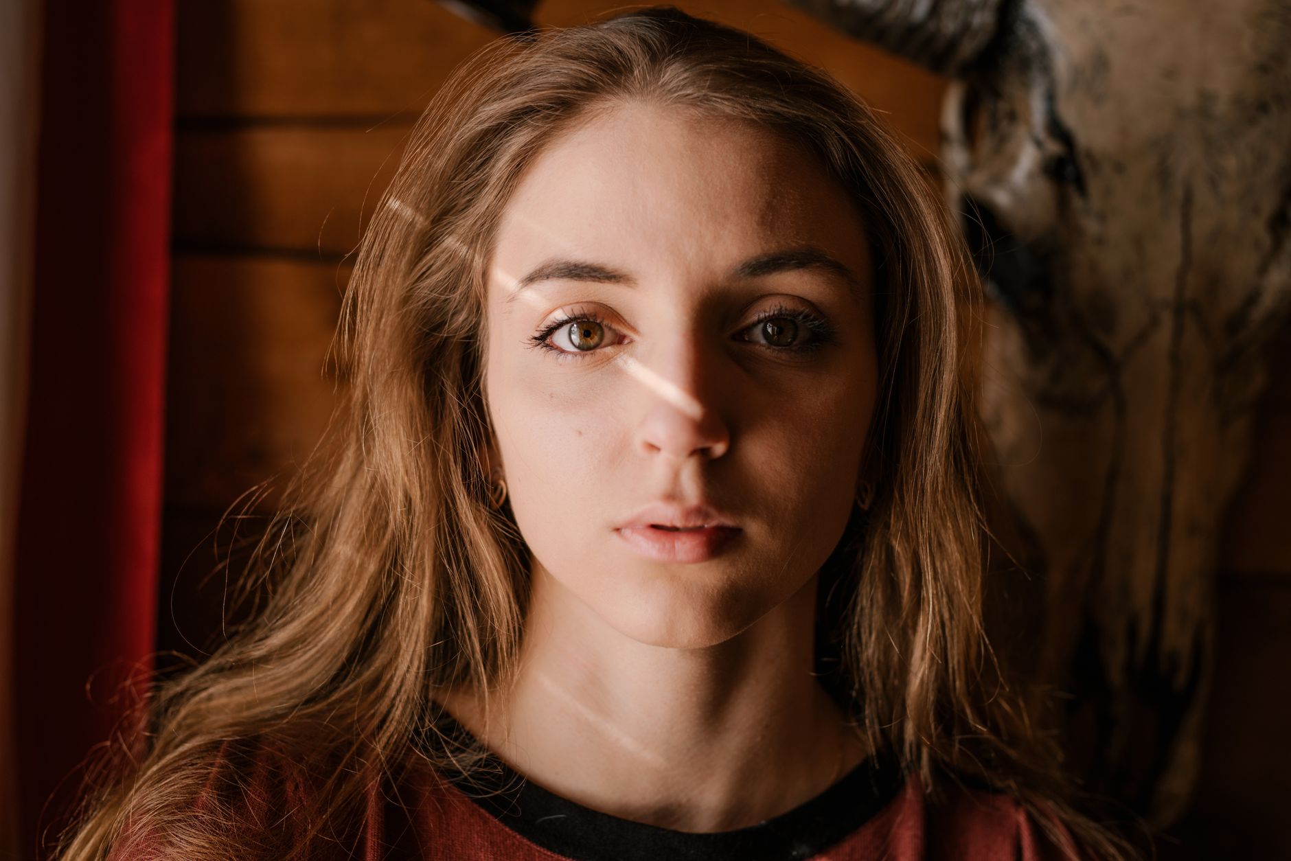Close-up portrait of a young woman with unique lighting and deer head in the background.