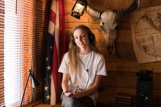 A woman sitting indoors, wearing headphones, enjoying music against a rustic background with a deer skull and vintage decor.