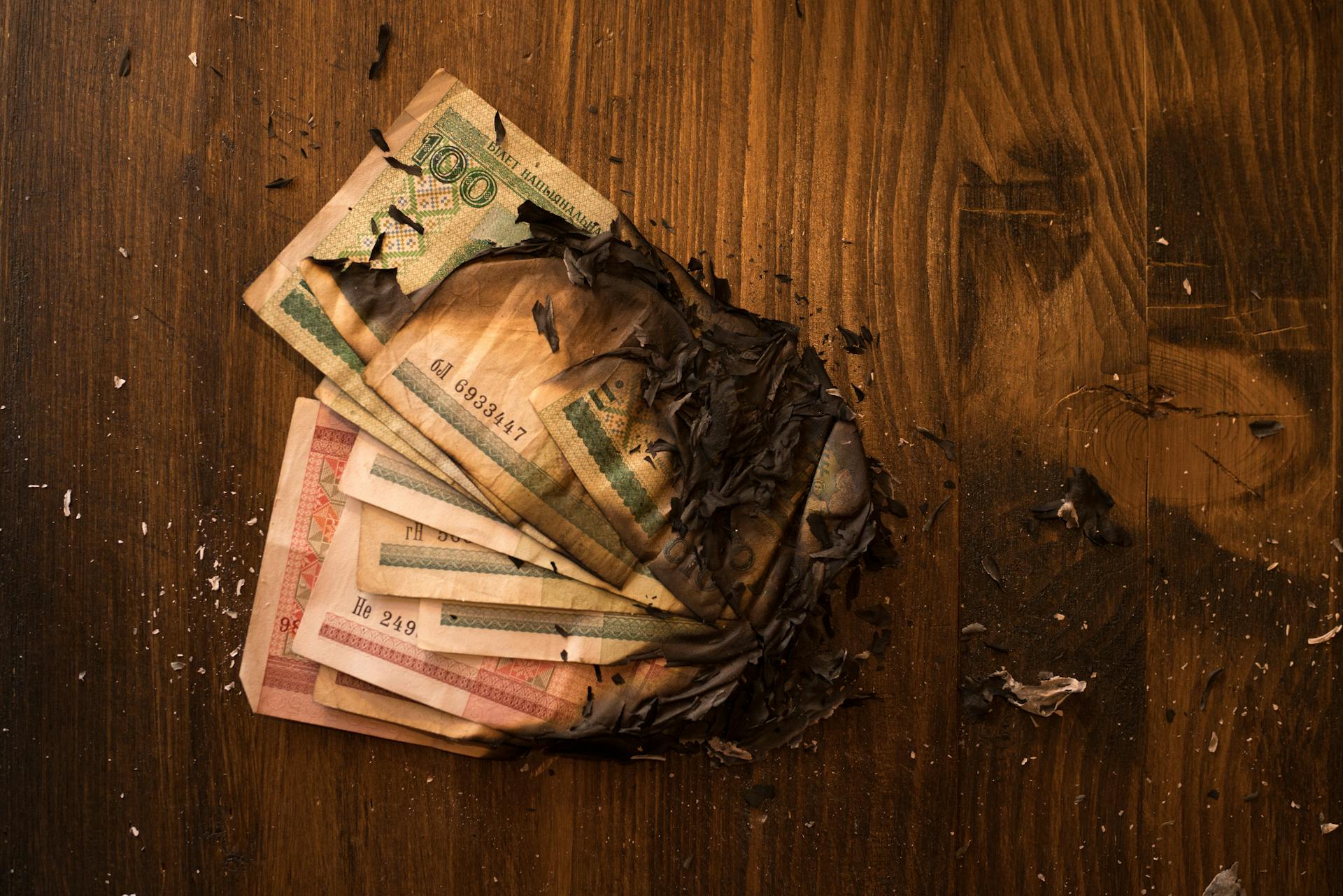 Scorched banknotes scattered on a dark wooden table, symbolizing financial loss.