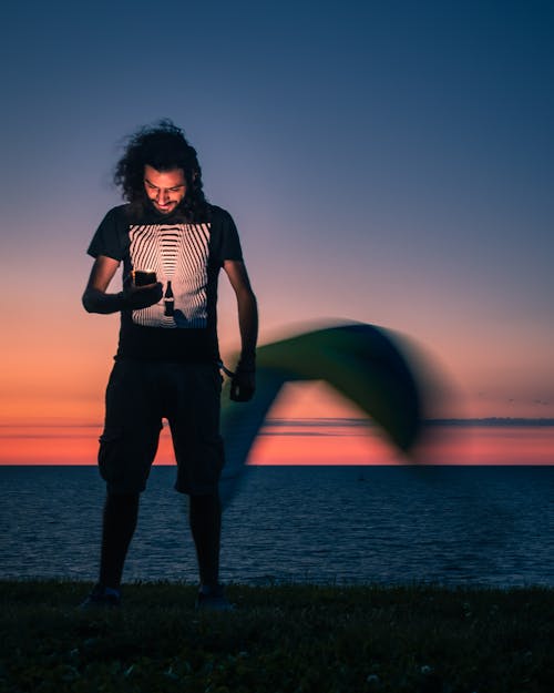 Man Standing at Seashore and Looking at his Smart Phone