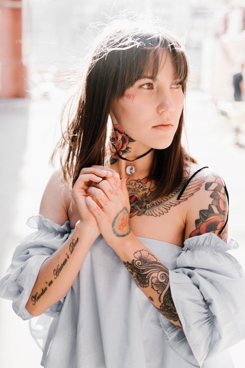 Free Portrait of a woman with colorful tattoos wearing a light blouse, looking pensive outdoors. Stock Photo