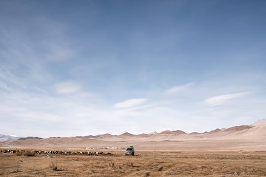 A lone vehicle navigates a remote desert landscape under a vast, clear blue sky.