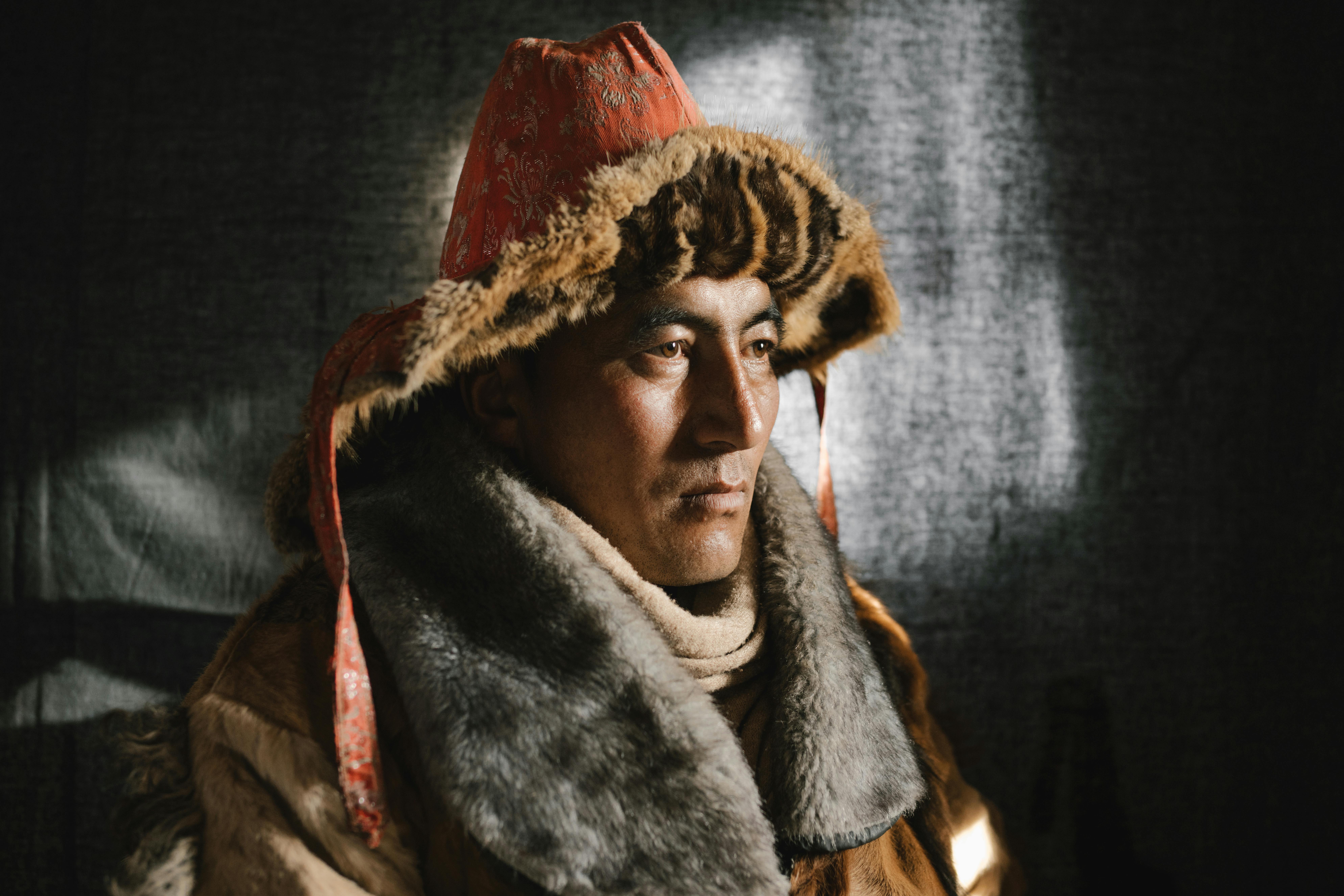 Close-up portrait of a man wearing a traditional fur hat and coat, gazing introspectively.