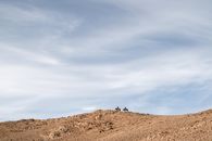 Person Standing on Brown Rock Mountain Under White Clouds and Blue Sky