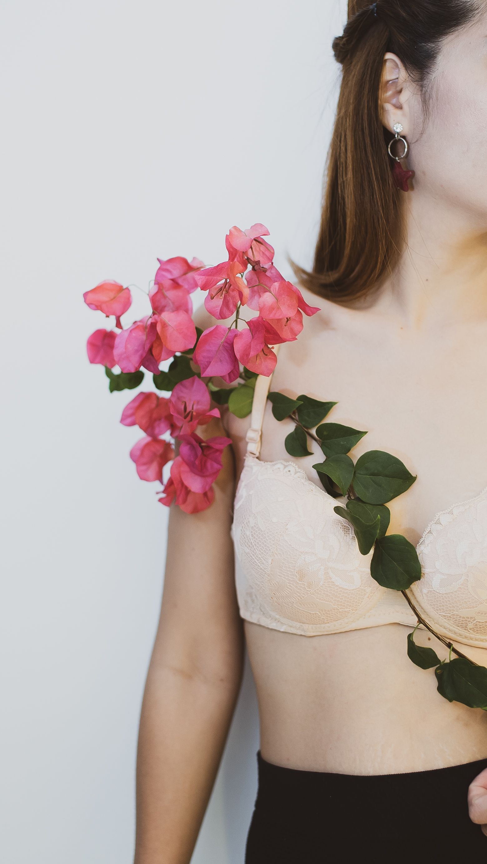 Artistic pose with delicate pink bougainvillea on a woman's shoulder, evoking a soft, elegant style.