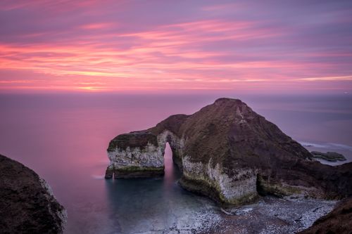 Free Serene seascape featuring a natural arch at sunset with pink and purple skies. Stock Photo
