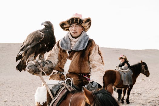 A Mongolian man in traditional attire practices falconry while horseback riding in a desert landscape.