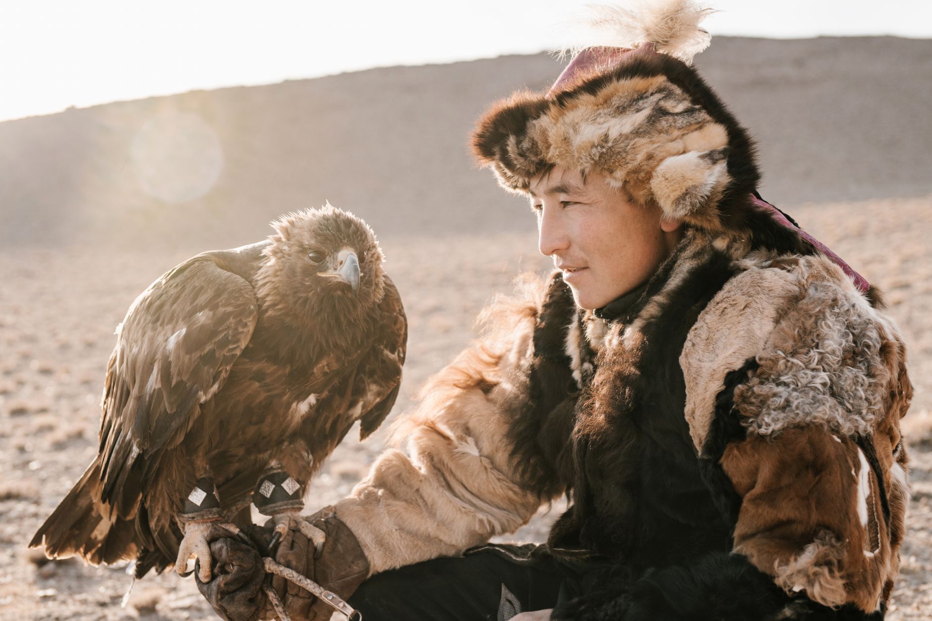 A Mongolian eagle hunter in fur attire with a golden eagle, showcasing traditional culture.