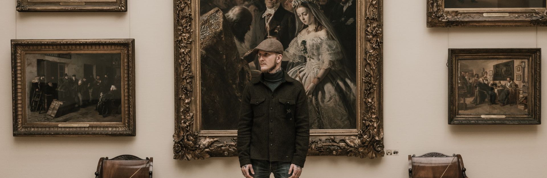 A man stands in a museum gallery surrounded by vintage paintings.