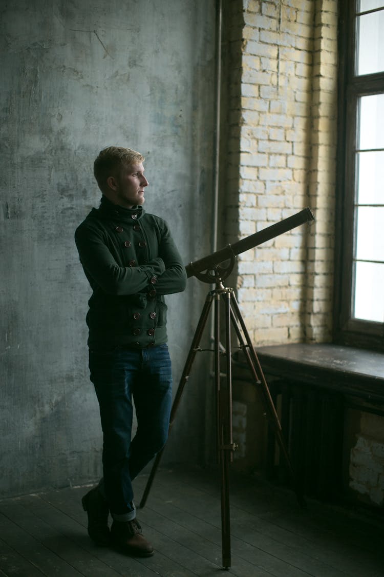 Man Standing In Empty Room With Vintage Telescope