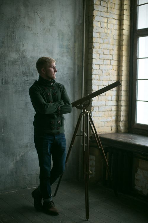 Free Man standing indoors beside vintage telescope and window with industrial decor. Stock Photo