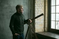 Man Standing Next to Telescope by Closed Window