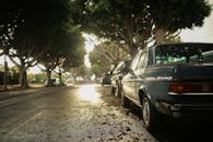 潮湿的街道上停着一辆老式汽车，绿树成荫，营造出一种宁静而略带忧郁的氛围