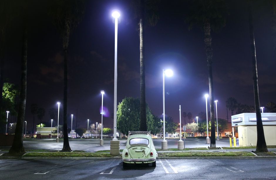A classic vintage car parked under bright street lights in an empty parking lot during nighttime.