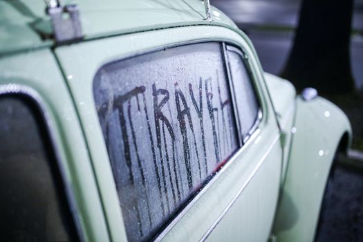 A retro car with a 'Travel' message written on foggy window at night.